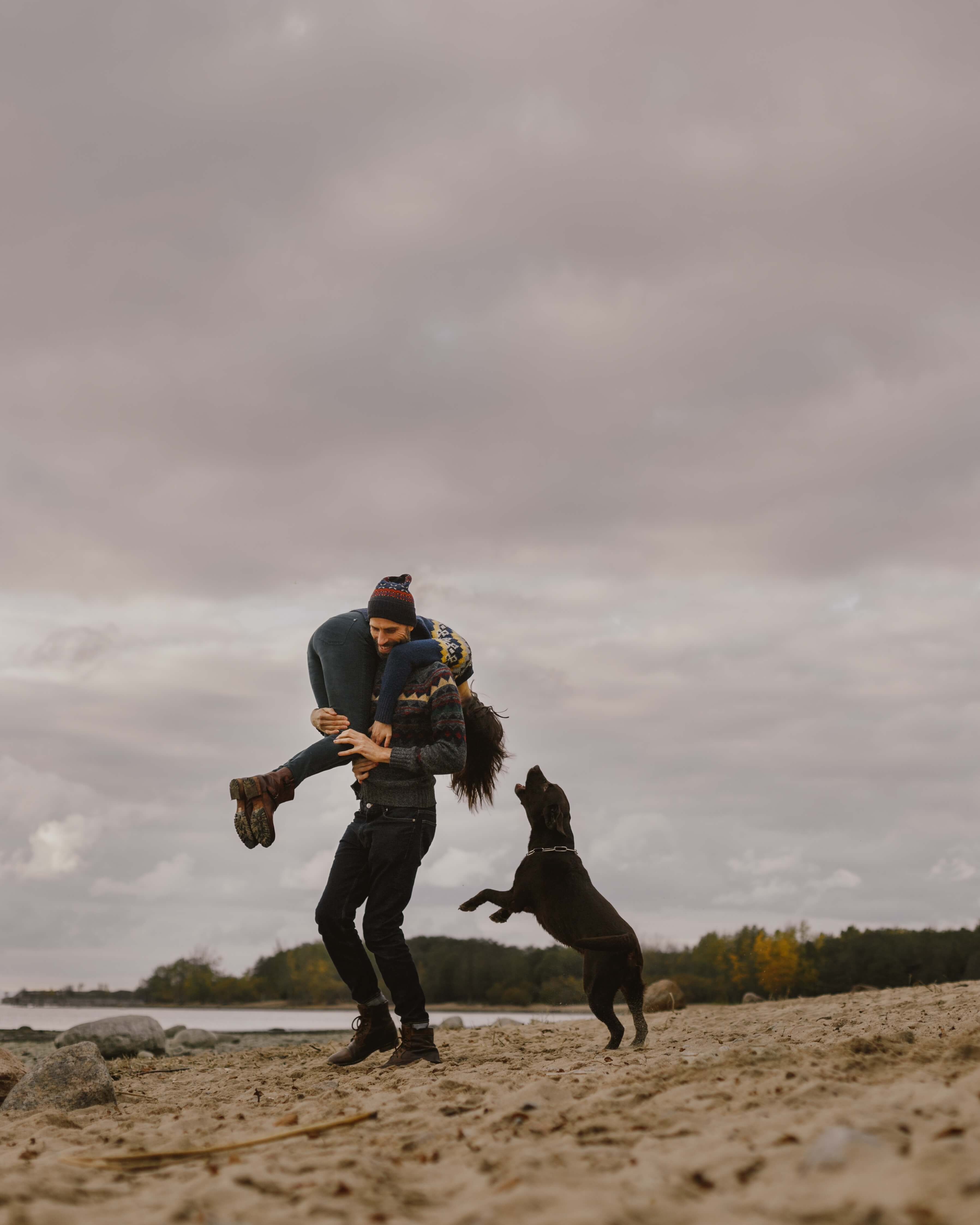 Man picking up woman while dog jumps