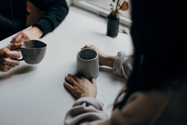 Man and woman sitting at a table across each other drinking coffee