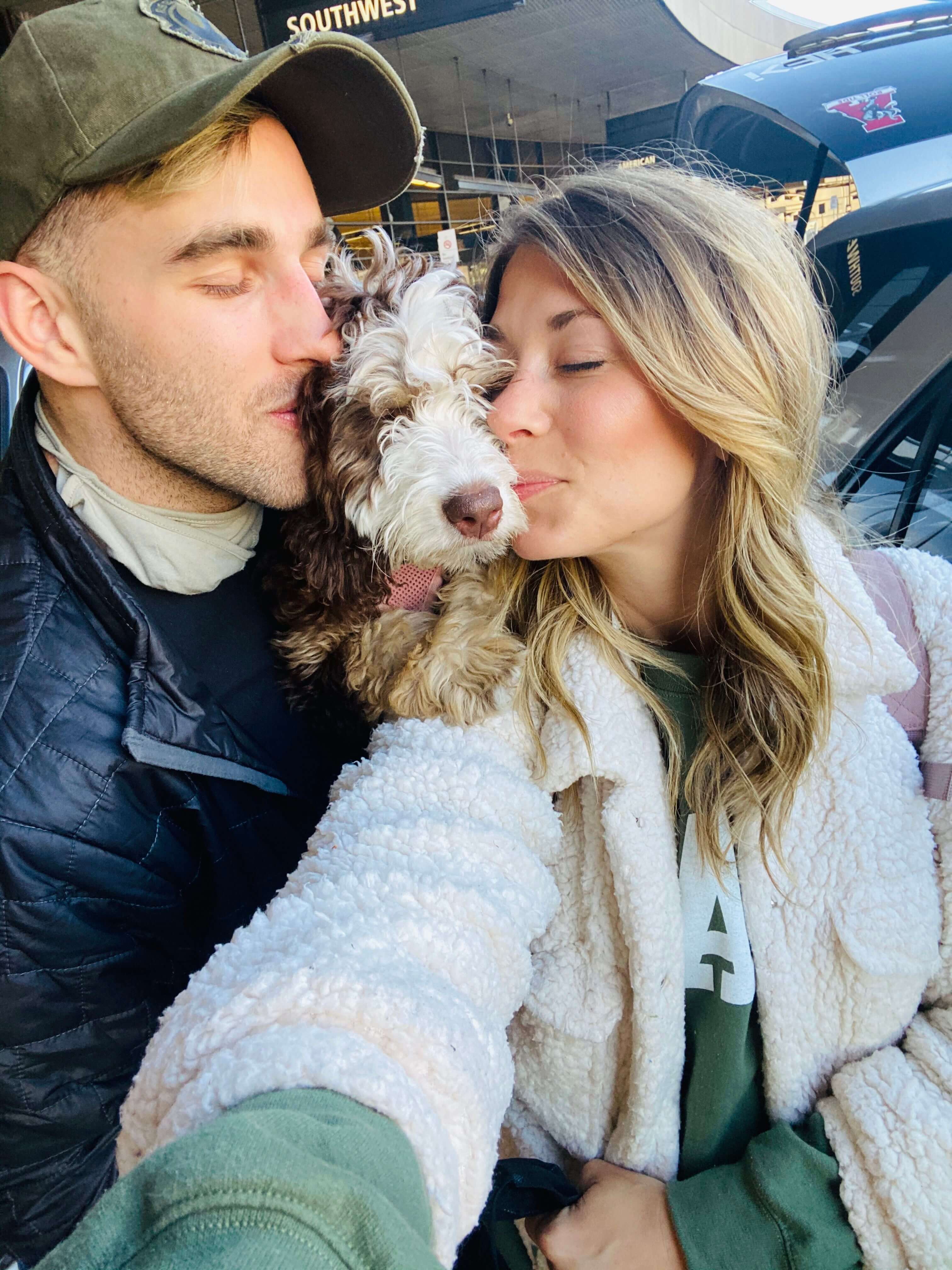JJ and Kait taking a selfie with them kissing their dog.
