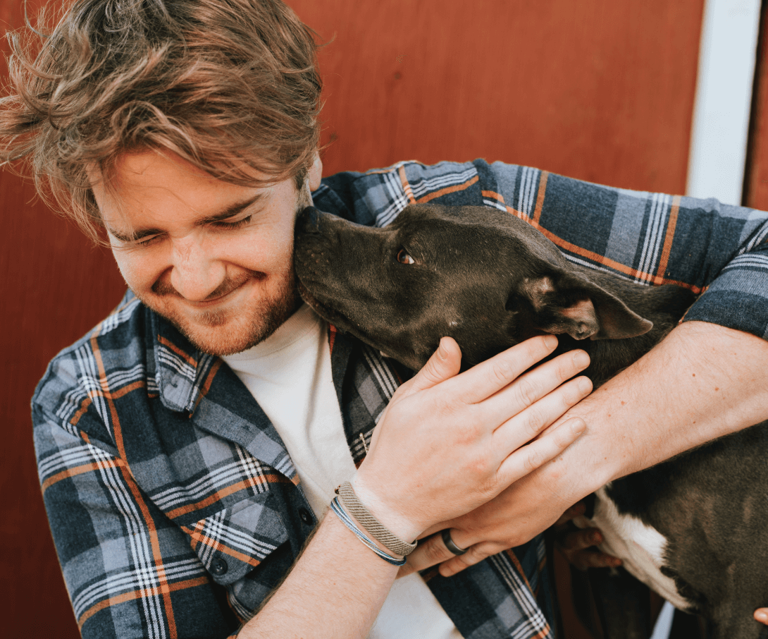 Man holding his dog while the dog licks his face