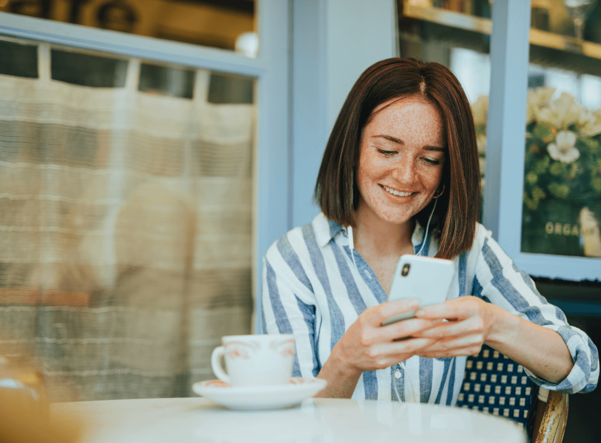 Woman sitting at coffee shot smiling and busy on her phone